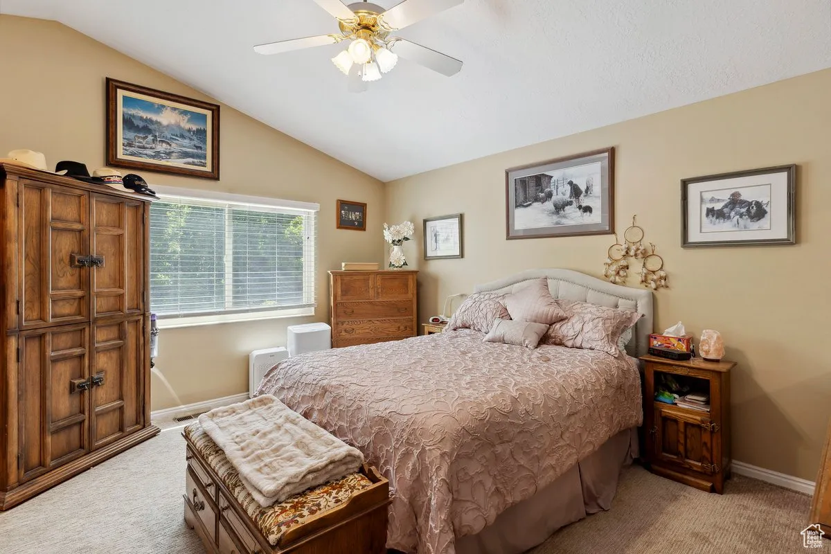 Bedroom featuring light carpet, lofted ceiling, baseboards, and a ceiling fan