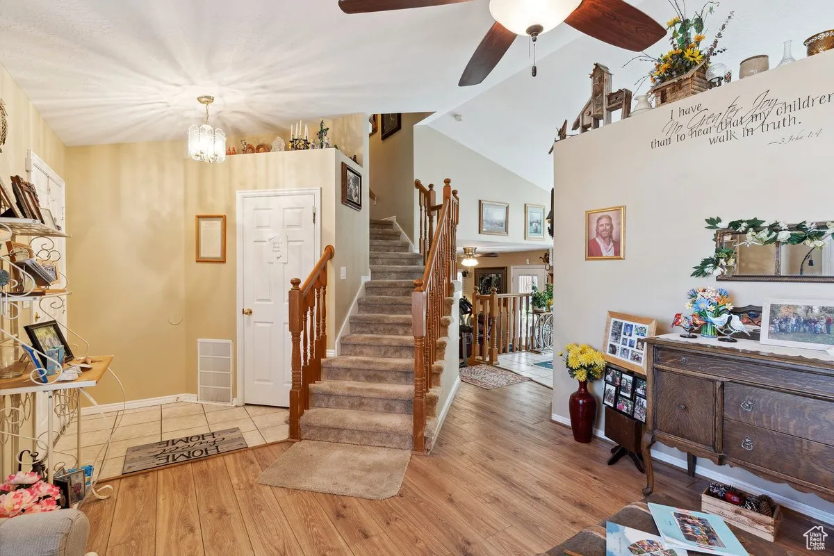 Entrance foyer with a ceiling fan, stairs, wood finished floors, baseboards, and vaulted ceiling