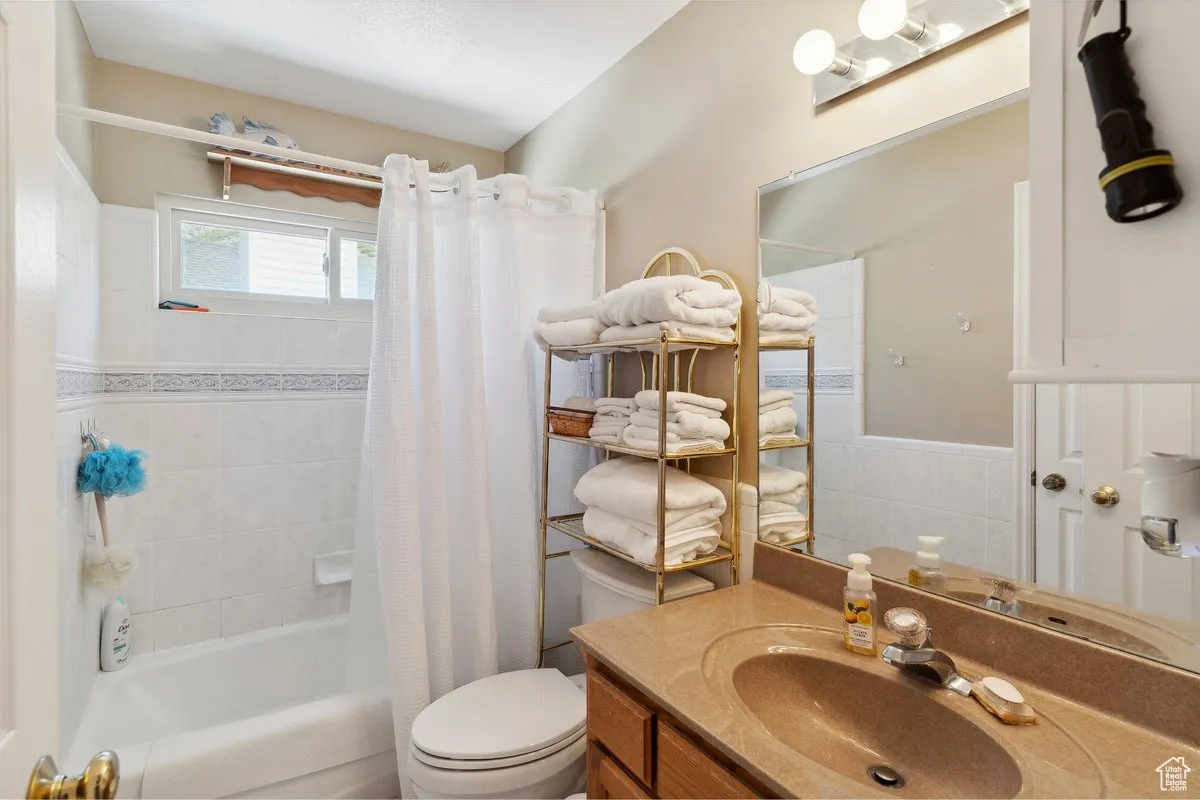 Full bathroom featuring toilet, shower / tub combo with curtain, tile walls, vanity, and wainscoting