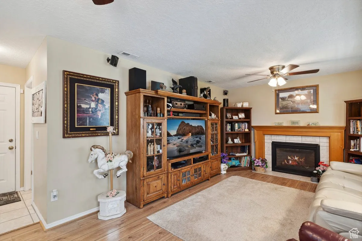 Living area featuring ceiling fan, wood finished floors, a tile fireplace, a textured ceiling, and baseboards