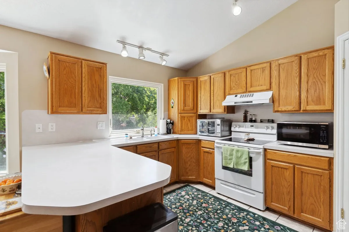Kitchen with electric stove, a peninsula, under cabinet range hood, track lighting, and lofted ceiling