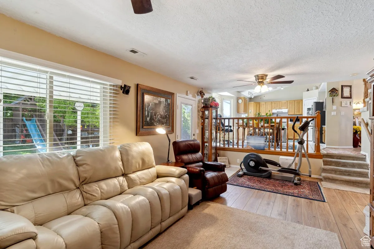 Living room with a ceiling fan, plenty of natural light, a textured ceiling, light wood-style flooring, and baseboards
