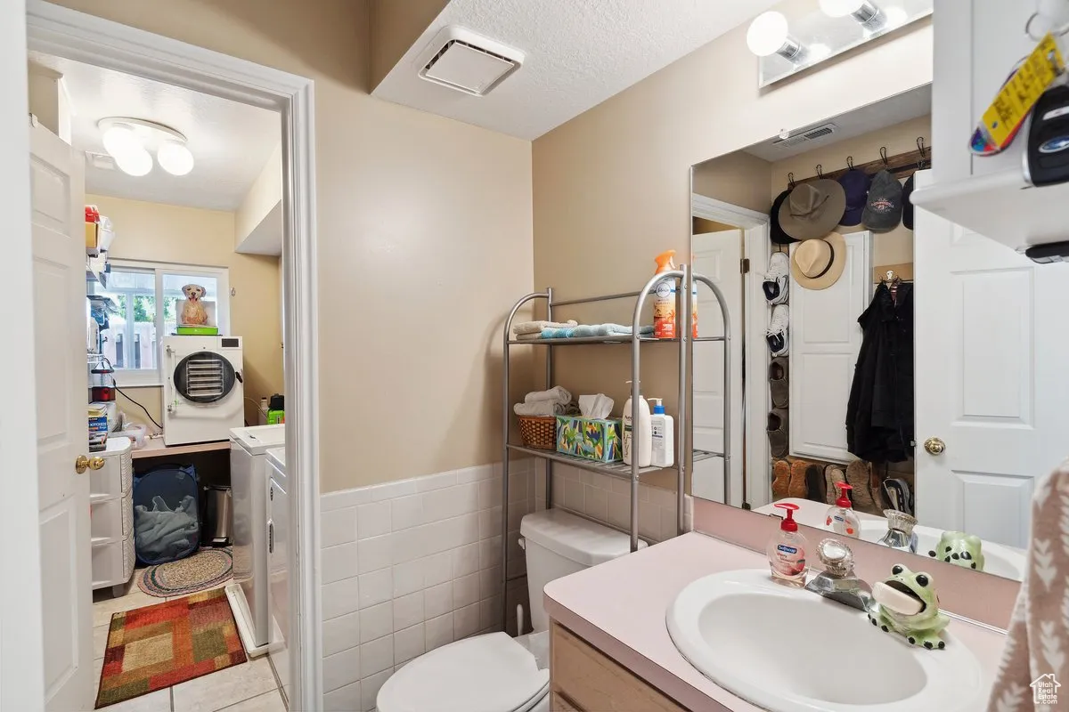 Bathroom with separate washer and dryer, toilet, vanity, tile patterned floors, and a wainscoted wall
