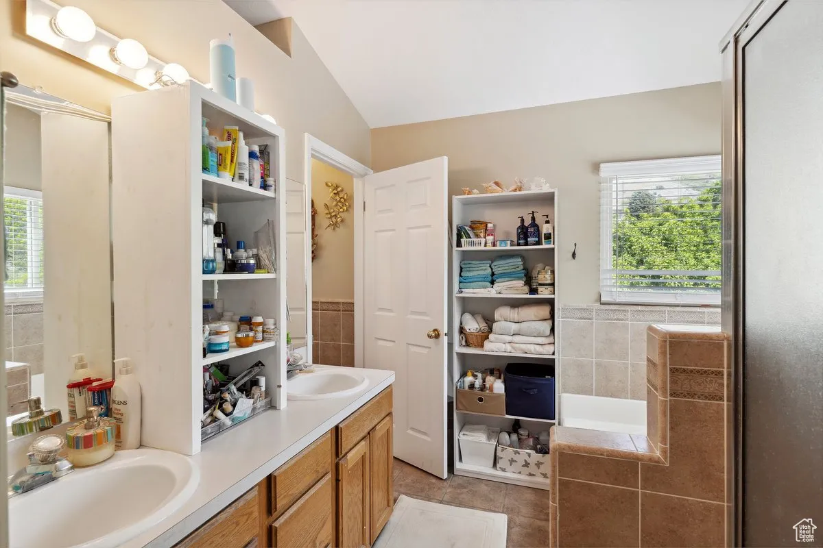 Full bathroom with healthy amount of natural light, lofted ceiling, tile patterned flooring, tile walls, and double vanity