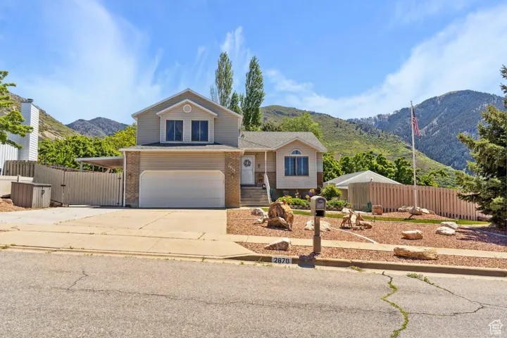 View of front facade featuring a mountain view, an attached garage, fence, concrete driveway, and brick siding