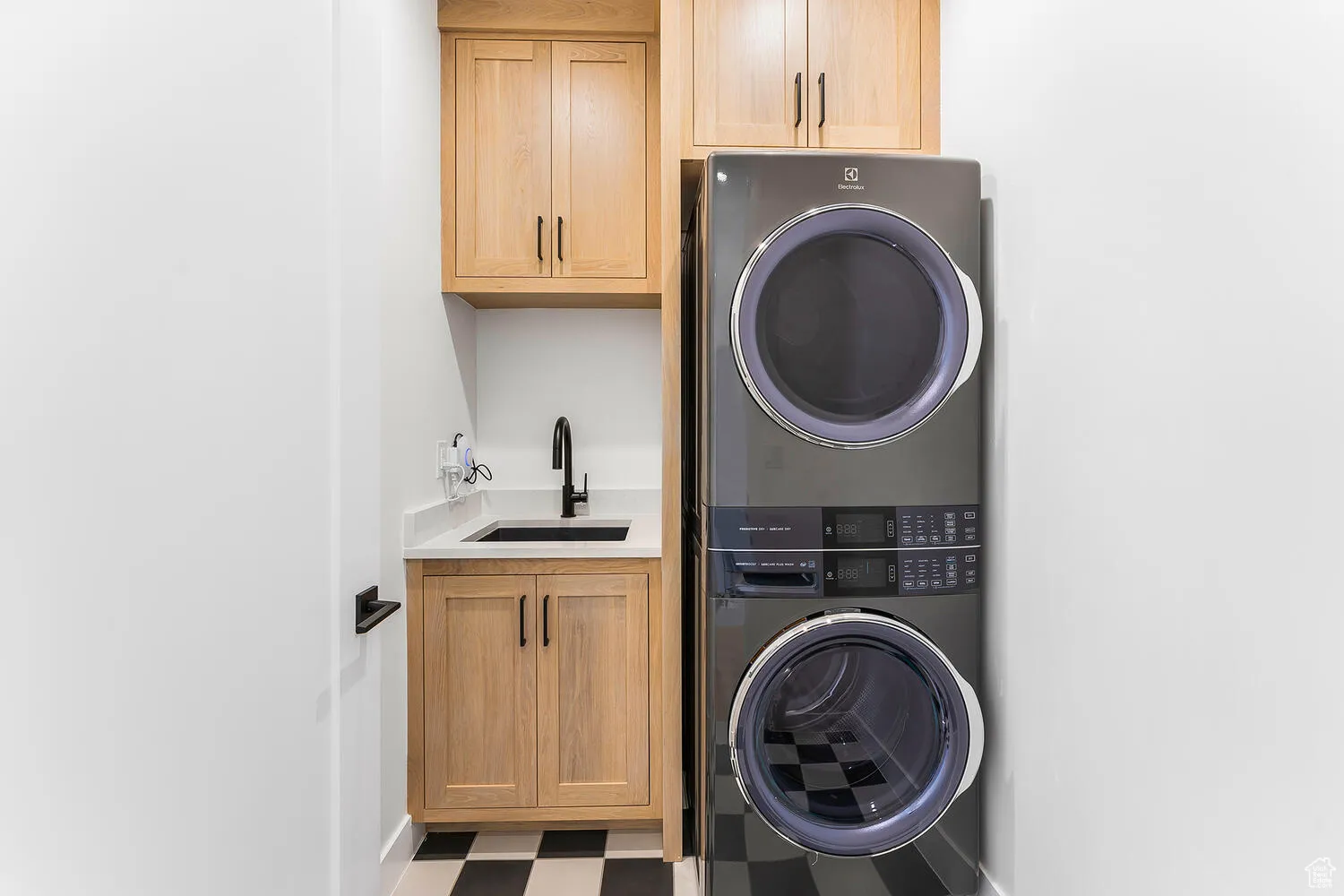 Washroom featuring stacked washer and clothes dryer, cabinet space, tile patterned floors, and baseboards