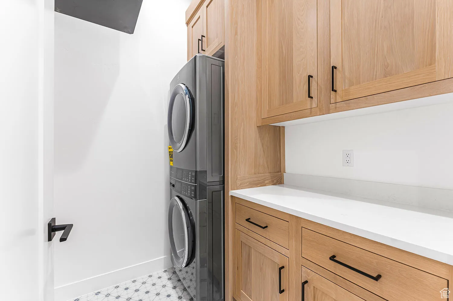 Laundry area with stacked washer / dryer, cabinet space, baseboards, and light flooring