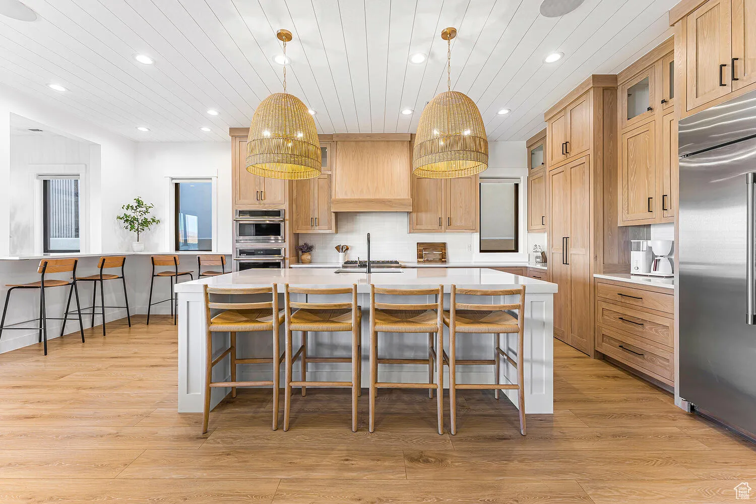 Kitchen with stainless steel appliances, light countertops, a kitchen breakfast bar, light brown cabinets, and recessed lighting