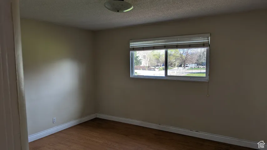 Unfurnished room featuring baseboards, a textured ceiling, and wood finished floors