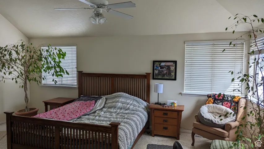 Bedroom with light colored carpet, vaulted ceiling, a ceiling fan, and baseboards