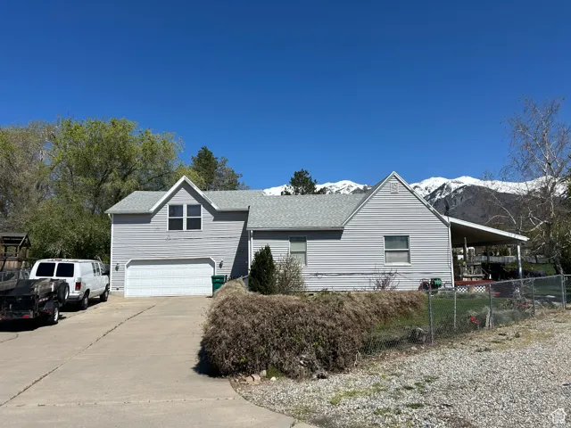 View of front facade with an attached garage, a shingled roof, a mountain view, driveway, and fence