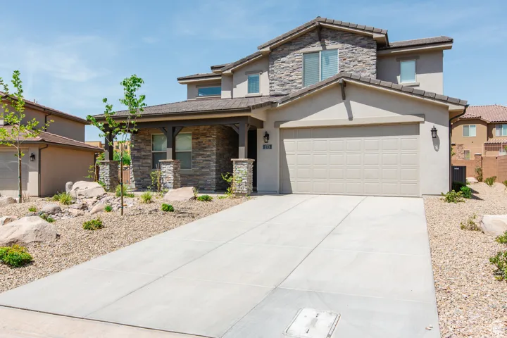 View of front facade with stone siding, driveway, stucco siding, and a tile roof