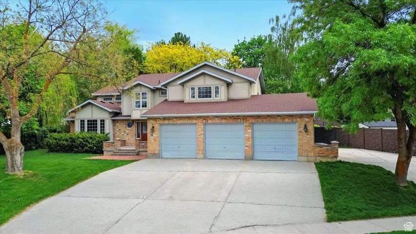 View of front of house featuring driveway, an attached garage, roof with shingles, brick siding, and stucco siding