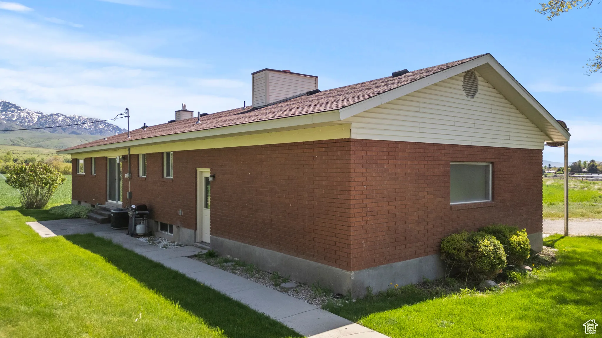 View of side of home featuring entry steps, brick siding, a lawn, a chimney, and a mountain view