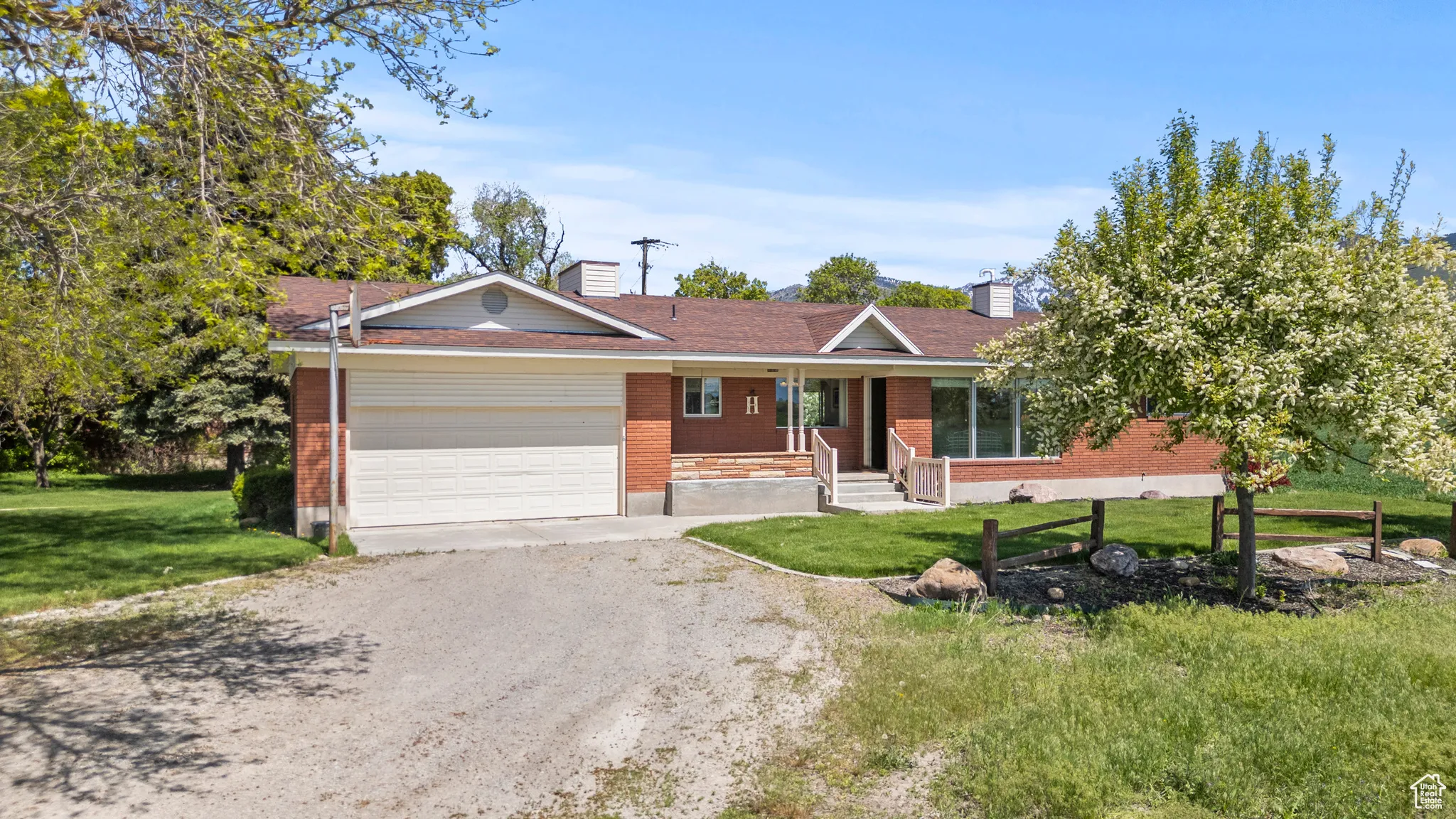 Single story home with a porch, dirt driveway, a garage, brick siding, and a front lawn