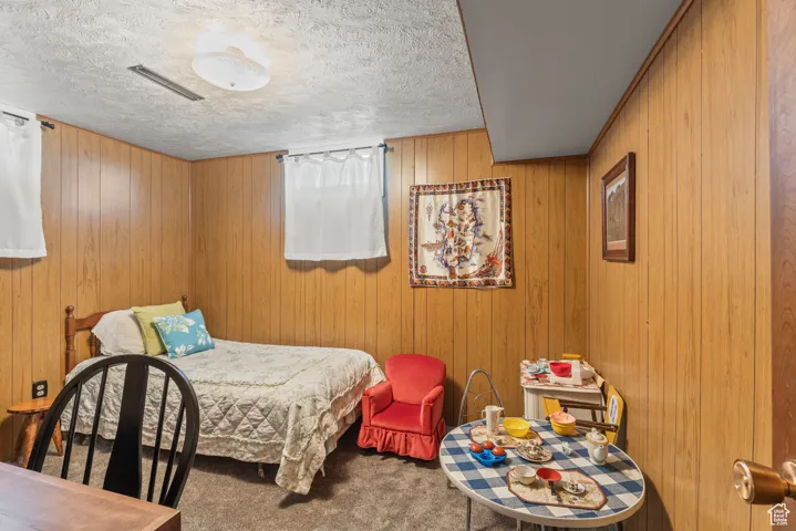Carpeted bedroom featuring a textured ceiling and wooden walls
