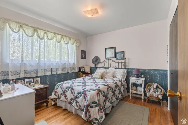 Bedroom featuring wallpapered walls, wood finished floors, and wainscoting