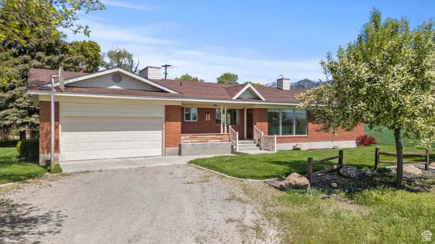 Ranch-style home with an attached garage, brick siding, a porch, dirt driveway, and a chimney