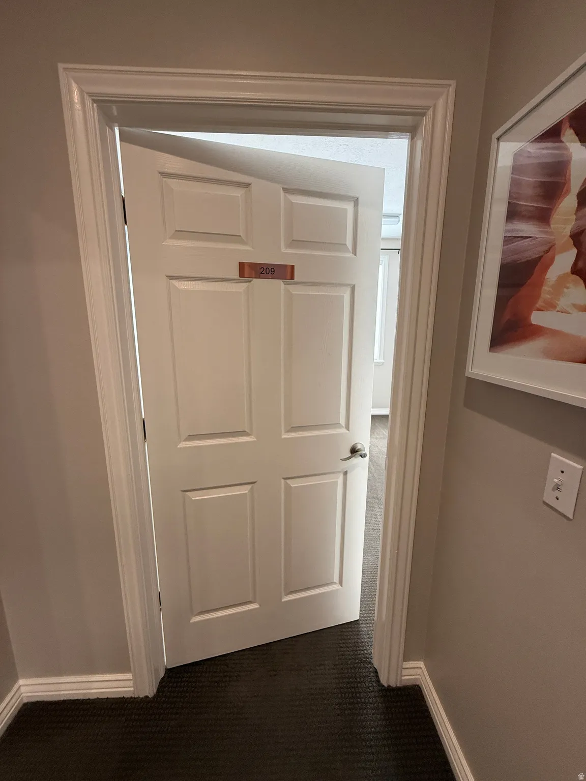 Hallway with baseboards and dark colored carpet