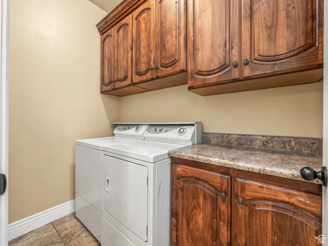Clothes washing area with washing machine and dryer, cabinet space, and baseboards