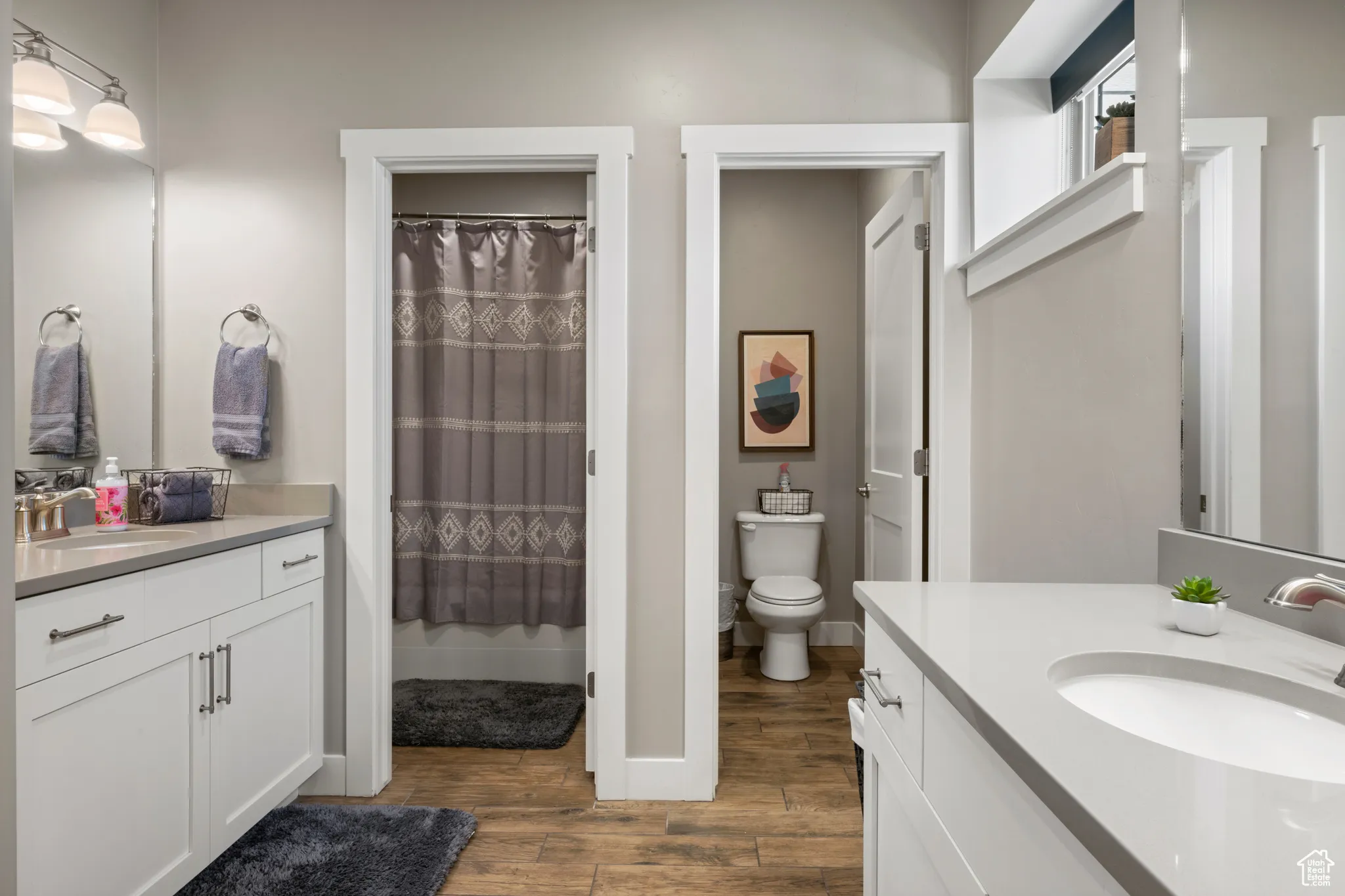 Full bath with wood finished floors, two vanities, and a shower with curtain