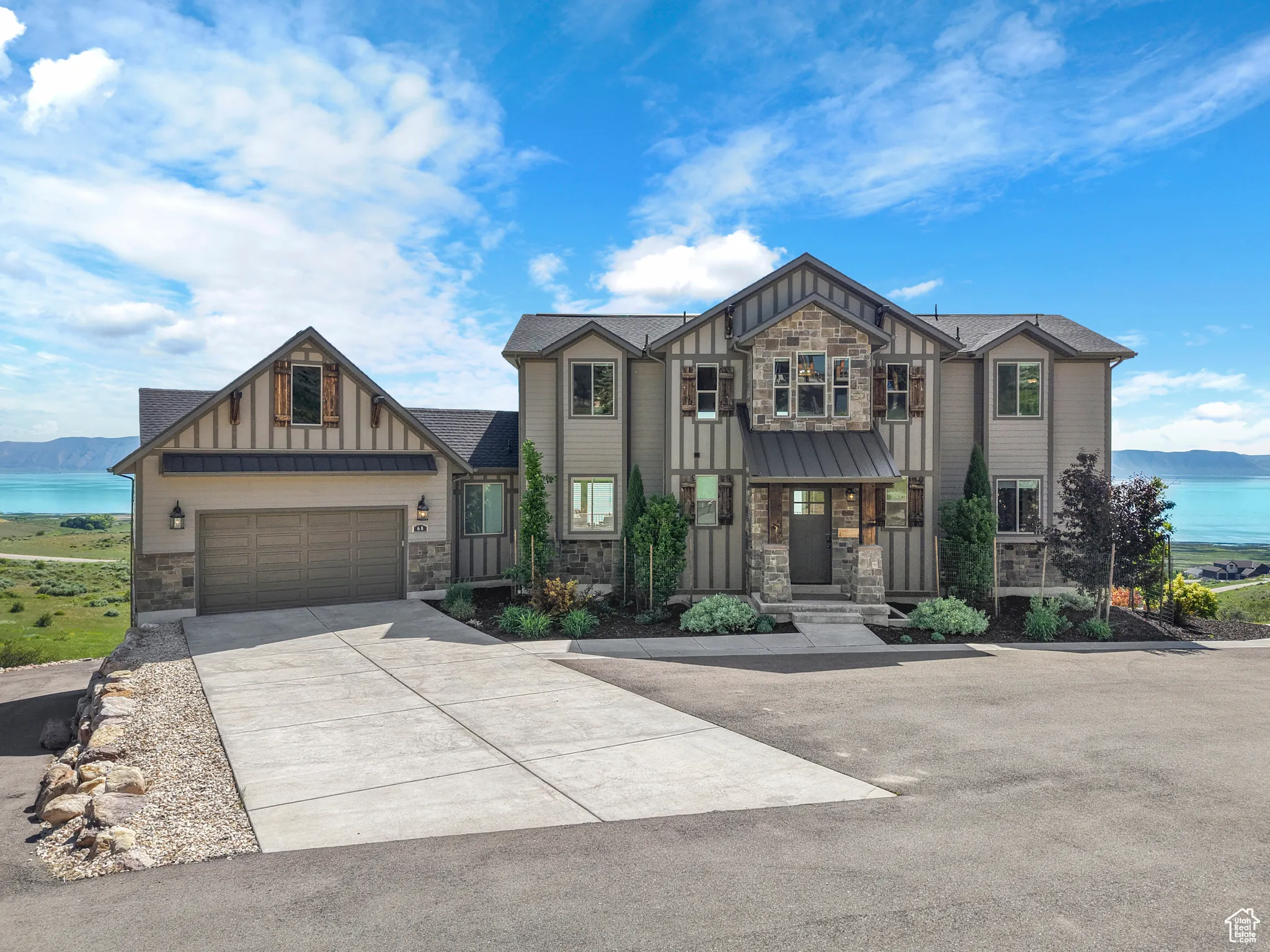 View of front of home featuring stone siding, board and batten siding, concrete driveway, and a water view