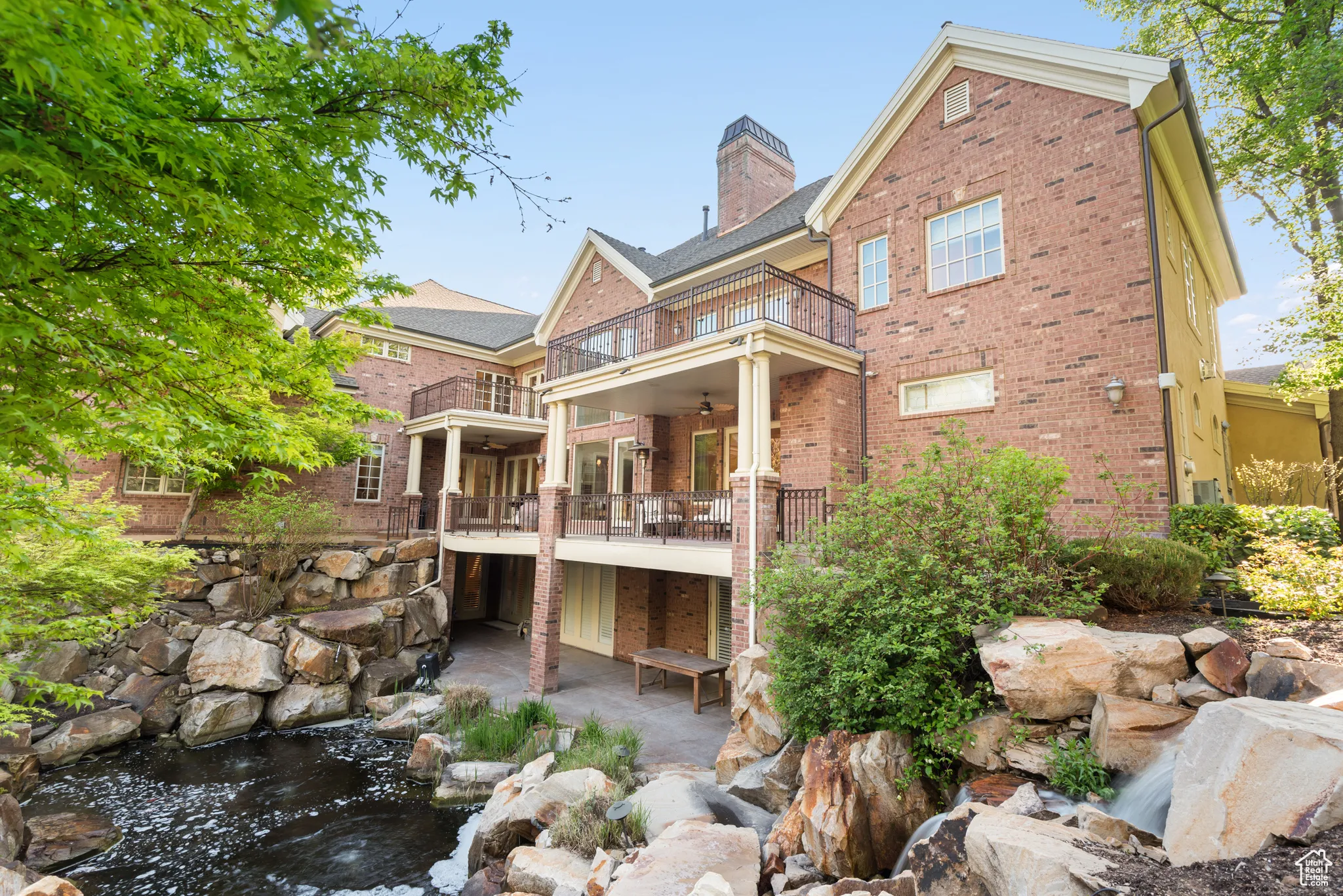 Rear view of property featuring a balcony, brick siding, ceiling fan, a chimney, and a garden pond
