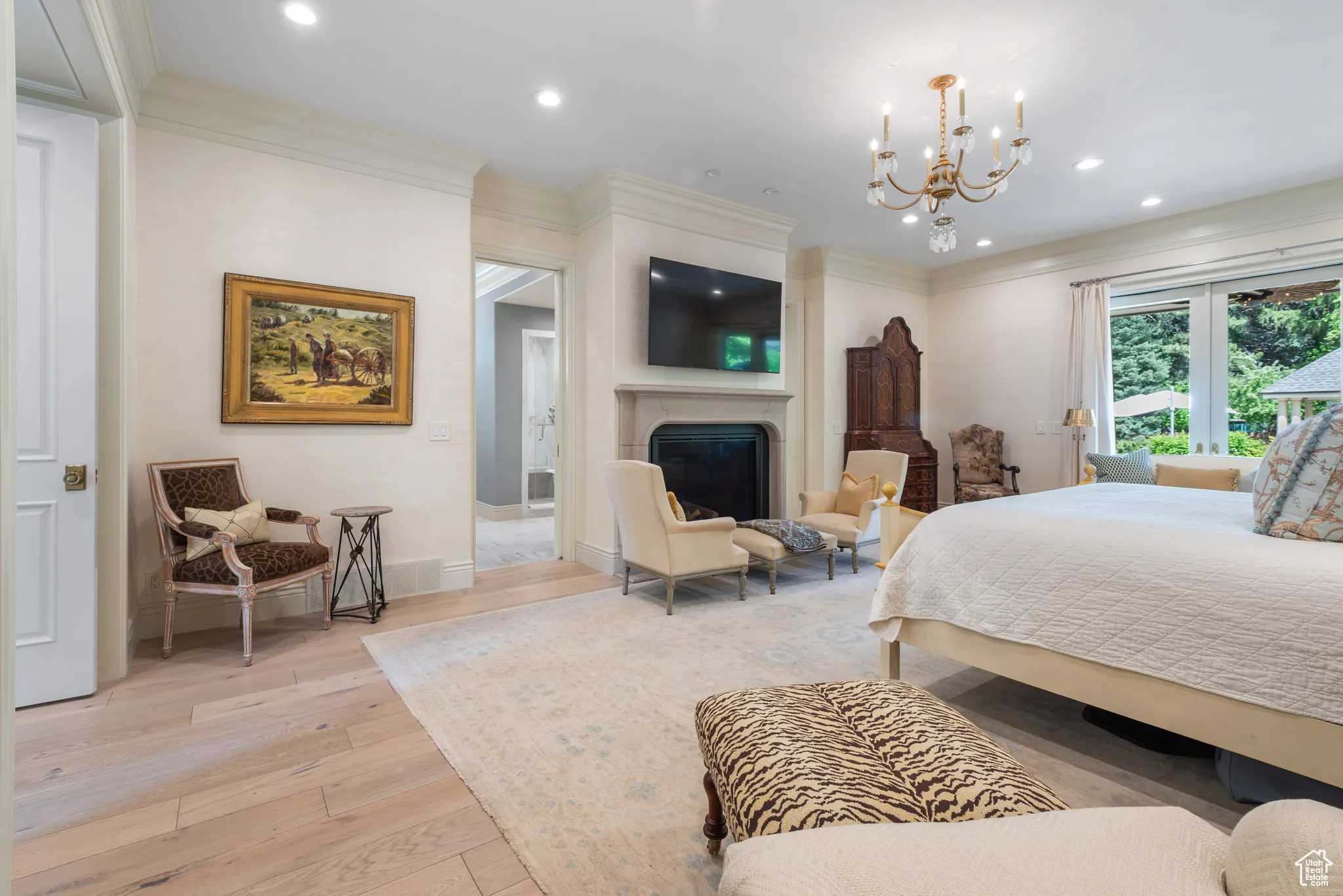 Bedroom featuring light wood finished floors, a glass covered fireplace, a chandelier, recessed lighting, and ornamental molding