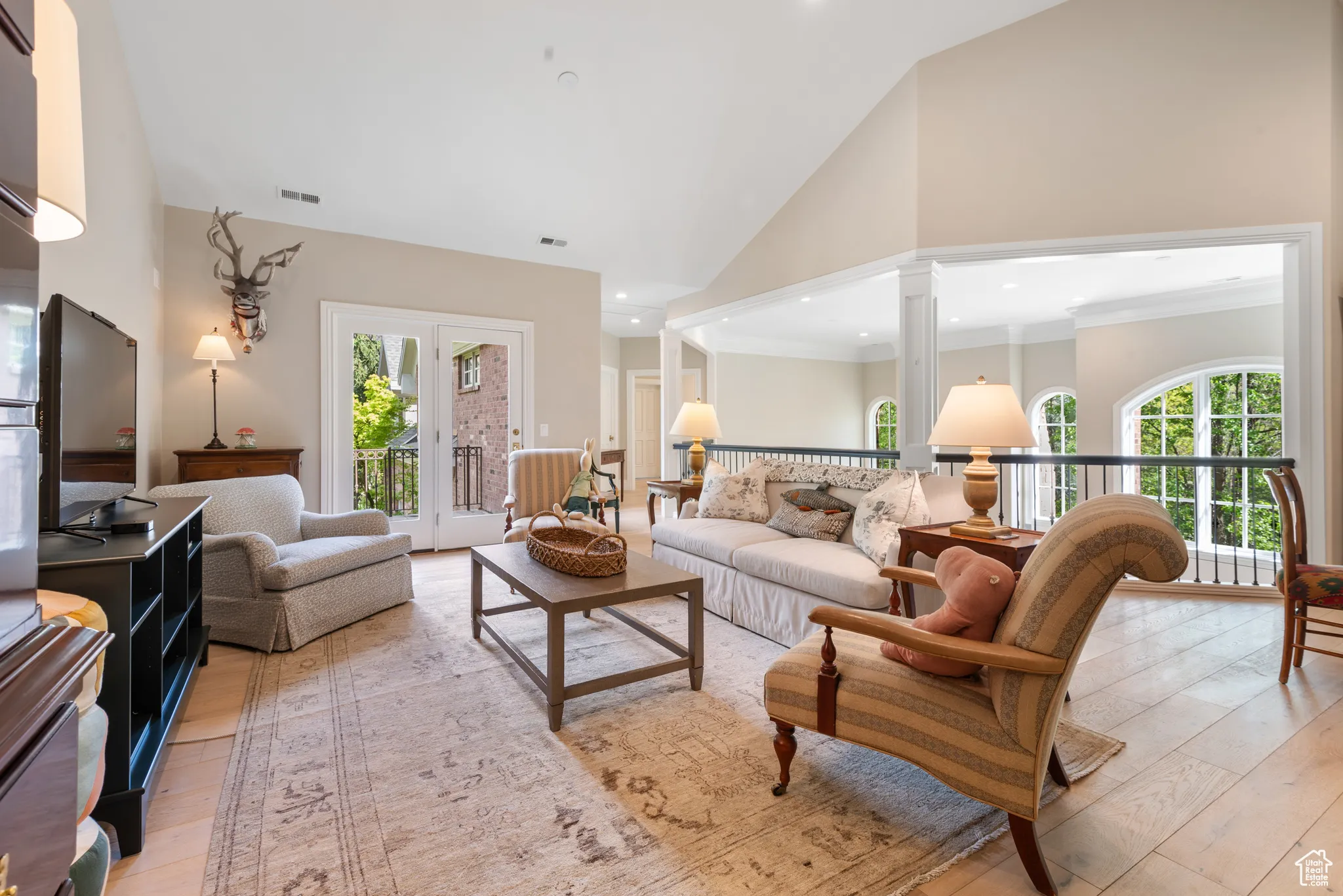 Living room with light wood-style flooring, high vaulted ceiling, decorative columns, ornamental molding, and recessed lighting