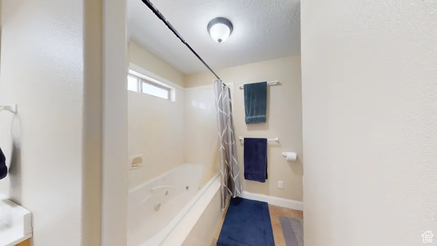 Bathroom featuring baseboards, a combined bath / shower with jetted tub, and a textured ceiling