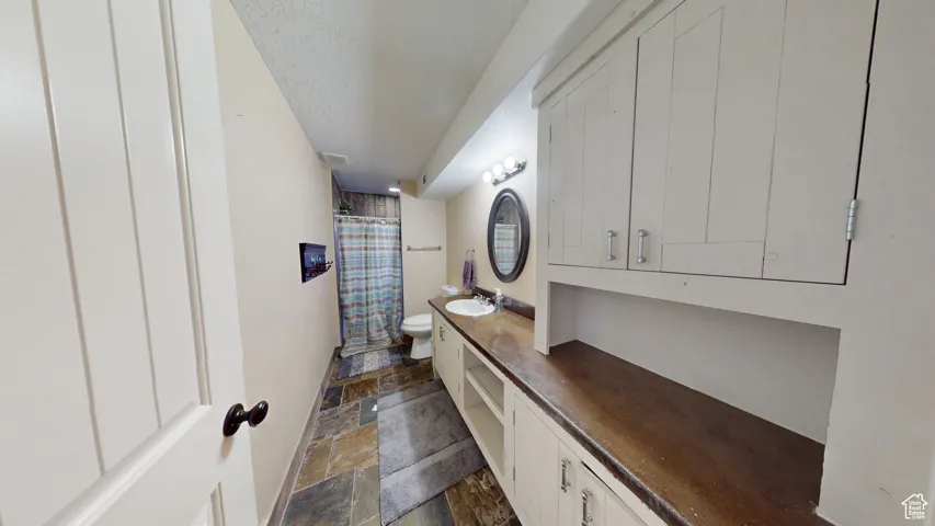 Bathroom featuring stone tile floors, toilet, vanity, curtained shower, and a textured ceiling