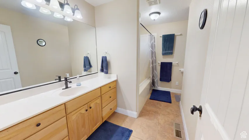 Full bath featuring vanity, shower / bathtub combination with curtain, tile patterned floors, and baseboards
