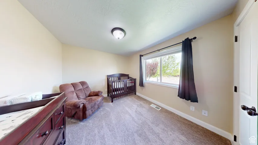 Bedroom featuring baseboards, light colored carpet, a textured ceiling, and a nursery area