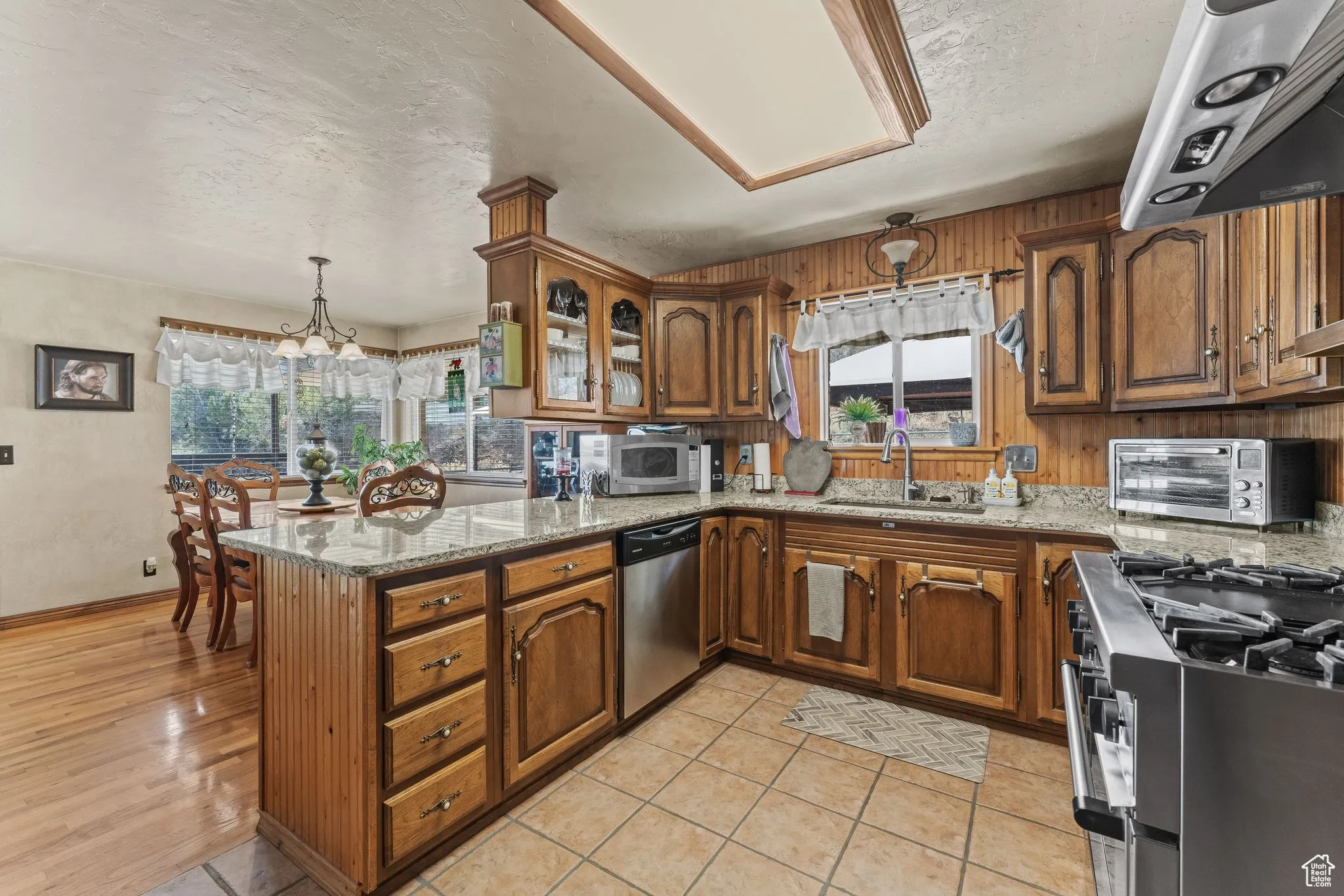 Kitchen featuring appliances with stainless steel finishes, a sink, brown cabinetry, a peninsula, and a textured ceiling