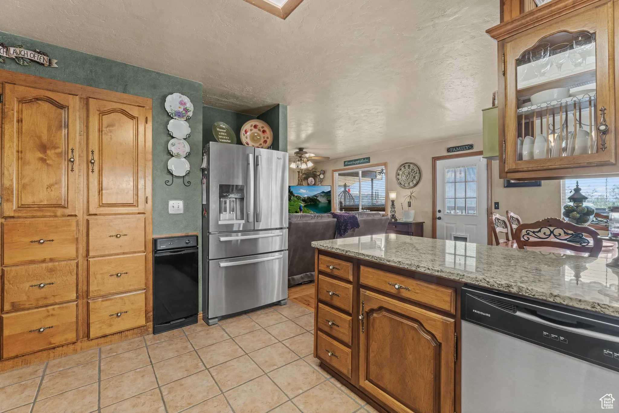 Kitchen featuring appliances with stainless steel finishes, healthy amount of natural light, light tile patterned floors, a textured ceiling, and brown cabinets