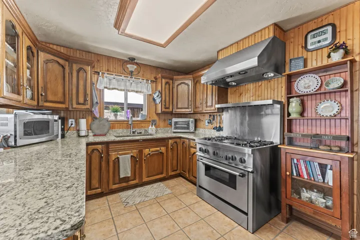 Kitchen with island exhaust hood, appliances with stainless steel finishes, brown cabinets, a sink, and wood walls