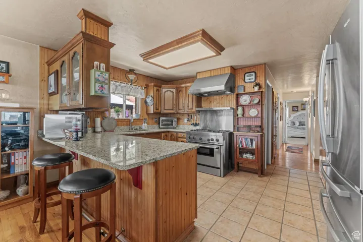 Kitchen with stainless steel appliances, wall chimney exhaust hood, a peninsula, a sink, and brown cabinets