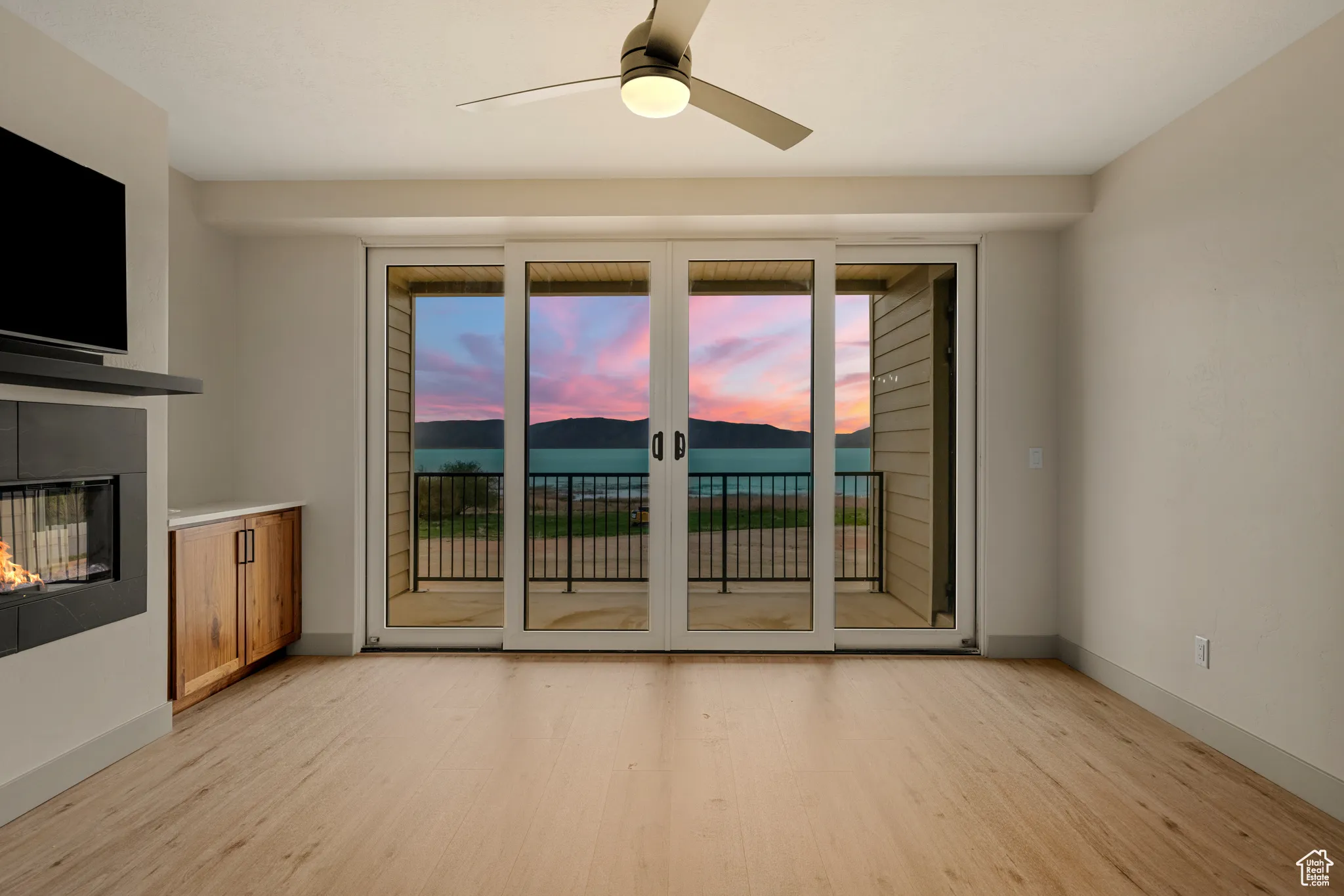 Unfurnished living room with light wood-style floors, a glass covered fireplace, a ceiling fan, and baseboards