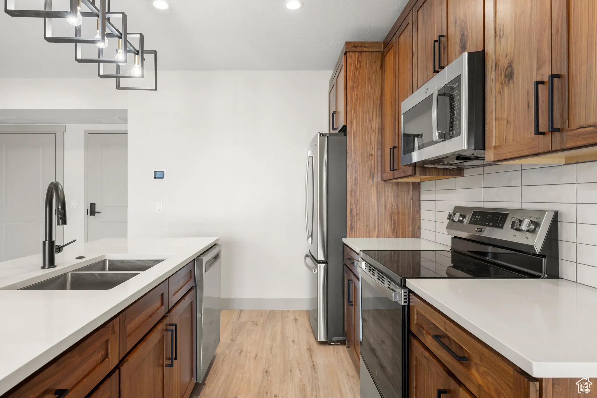 Kitchen with stainless steel appliances, a sink, light wood-type flooring, brown cabinetry, and recessed lighting