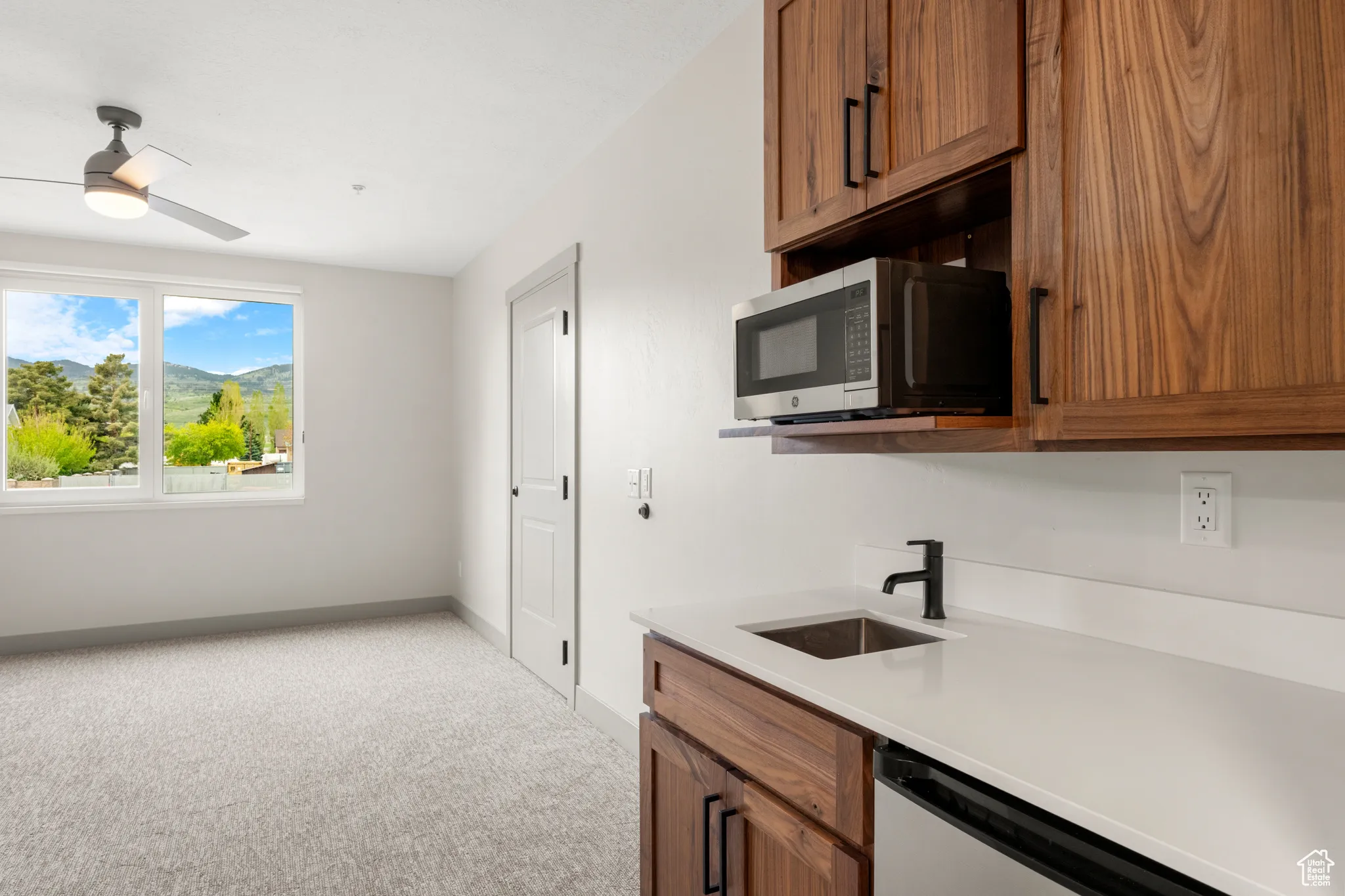 Kitchen featuring stainless steel microwave, a sink, light colored carpet, and brown cabinets