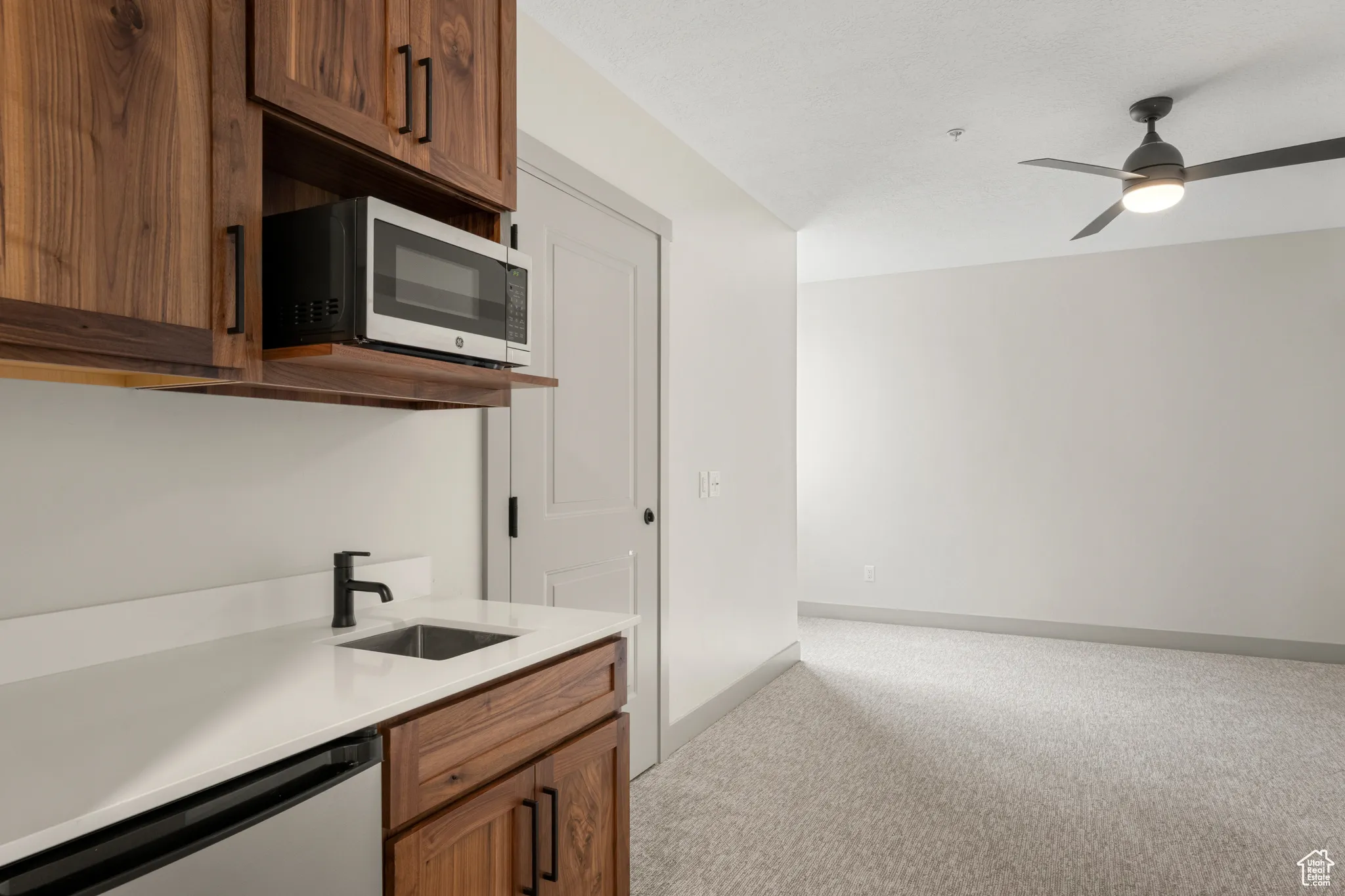 Kitchen featuring stainless steel appliances, light colored carpet, a sink, light countertops, and ceiling fan