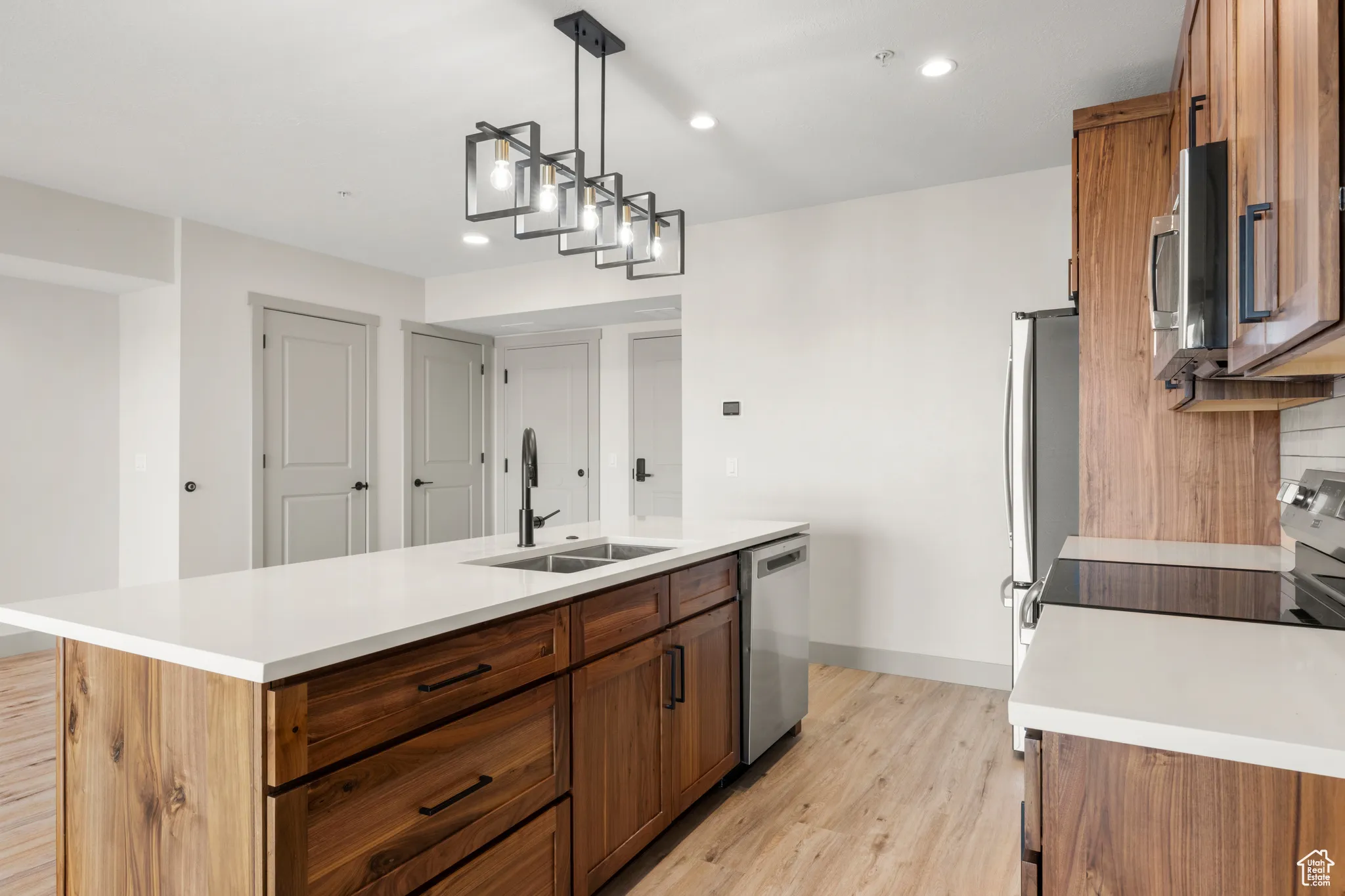Kitchen with a sink, stainless steel appliances, brown cabinetry, light wood-type flooring, and recessed lighting