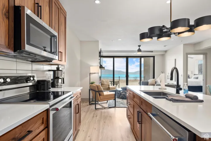 Kitchen featuring appliances with stainless steel finishes, a sink, open floor plan, brown cabinetry, and light wood-style flooring