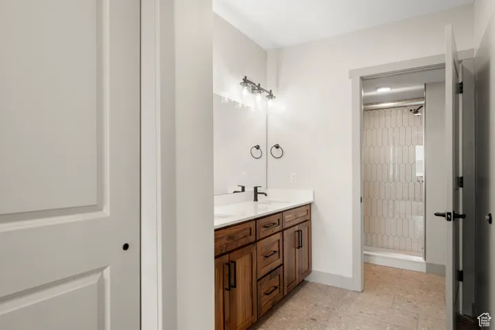 Full bathroom with a shower stall, double vanity, baseboards, and tile patterned floors
