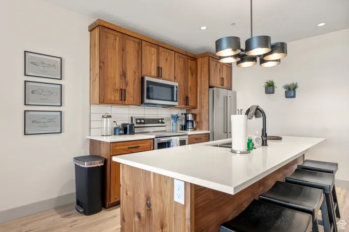 Kitchen with stainless steel appliances, light wood finished floors, brown cabinetry, a sink, and recessed lighting