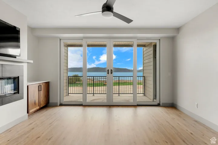 Unfurnished living room with light wood-style flooring, ceiling fan, a glass covered fireplace, and baseboards
