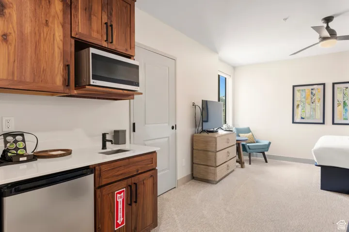 Kitchen with appliances with stainless steel finishes, light colored carpet, a sink, brown cabinetry, and baseboards