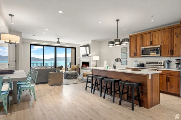 Kitchen featuring stainless steel appliances, brown cabinetry, a sink, light wood-style floors, and open floor plan