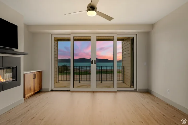 Unfurnished living room with light wood-style floors, a glass covered fireplace, a ceiling fan, and baseboards