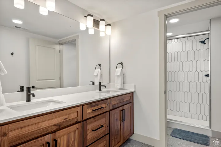 Bathroom with a tile shower, double vanity, baseboards, and recessed lighting